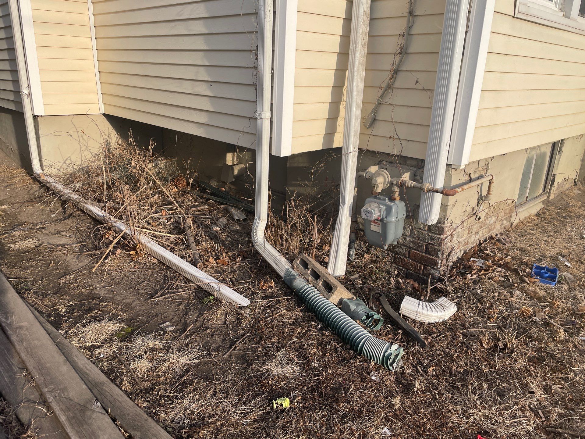 Epp Foundation Repair inspecting neglected exterior foundation with broken downspout, debris, and poor drainage in Des Moines