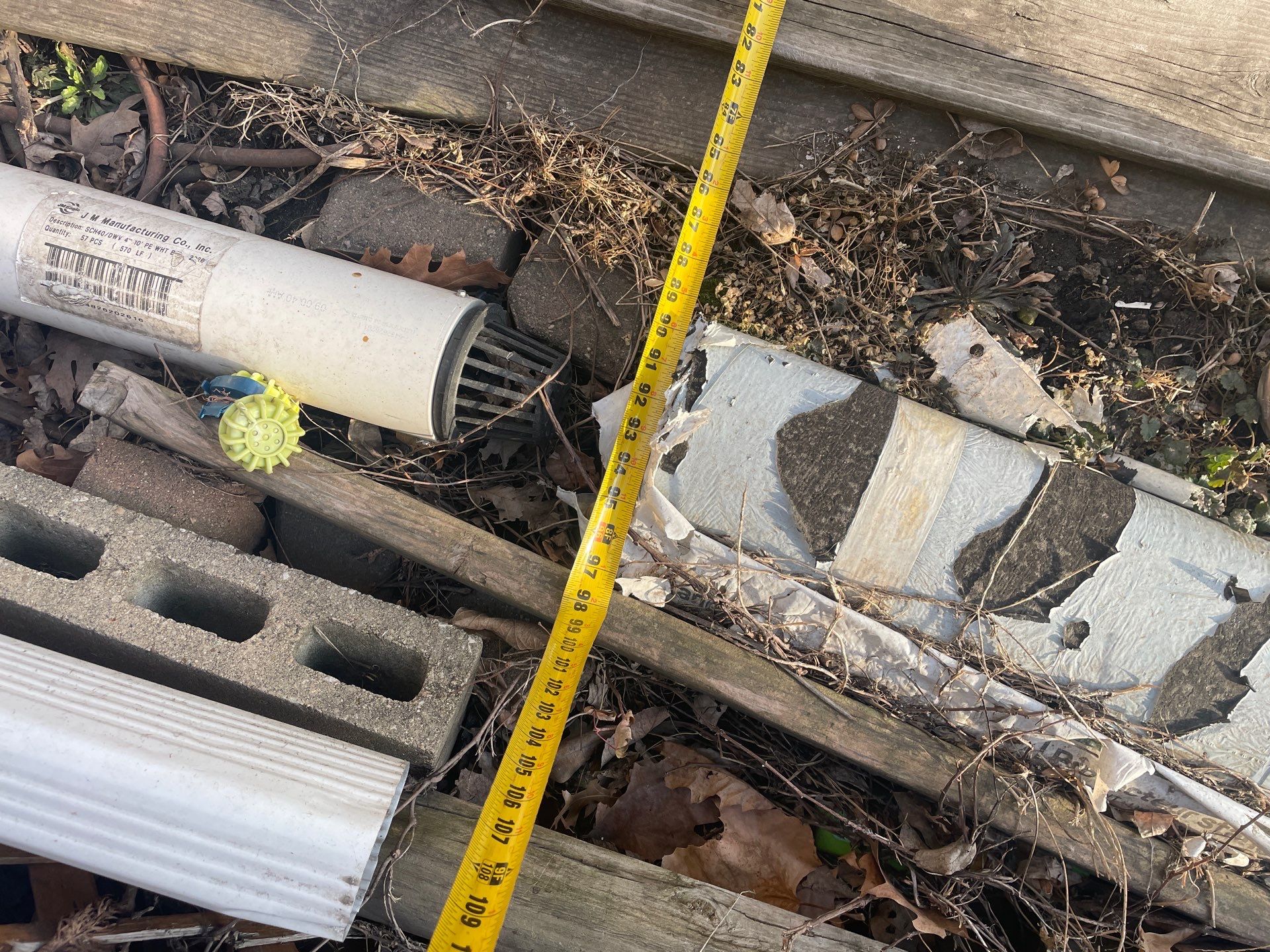Epp Foundation Repair assessing debris and drainage pipe with measuring tape in a crawl space, Des Moines, Iowa.